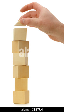 The hand establishes a toy roof on wooden cubes. Isolated on white Stock Photo