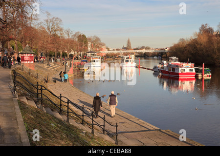 People walking along River Dee riverside walk with pleasure boats by boat landing stage. The Groves Chester Cheshire England UK Stock Photo