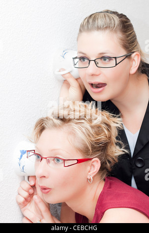 Two young Curious women listening through the wall. Stock Photo