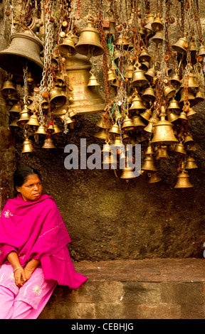 A lady resting under temple bells, India Stock Photo