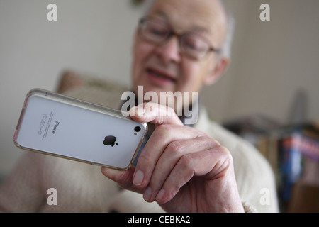 Elderly man adopting new technology, touchscreen iPhone, Smartphone, at home (photographers studio) Leiston, Suffolk, UK. Stock Photo