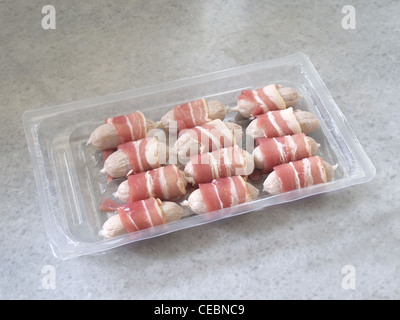 A Selection of Pigs In Blankets (sausages wrapped in bacon) in packaging on a marble slab Stock Photo