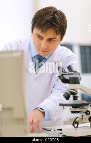 Researcher working in medical laboratory using microscope and computer Stock Photo
