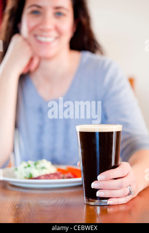 Young woman holding a pint with lunch at a pub Stock Photo