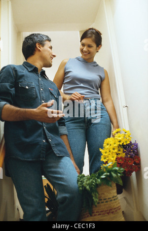 Couple standing on steps, talking, man holding basket of produce, woman carrying flowers Stock Photo