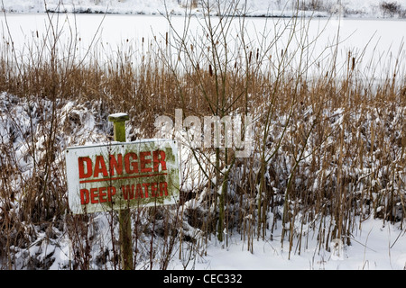 Danger deep water sign next to frozen pond in snow Stock Photo