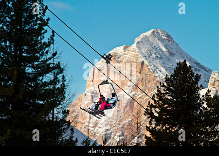 Skiers on a ski lift with Tofana di Rozes in the background, Faloria ski lift, Dolomites, Cortina d;Ampezzo, Italy Stock Photo