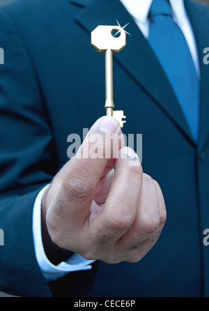 Businessman holding a shiny gold key Stock Photo