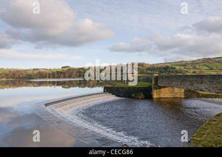 Water flowing over spillway weir from calm scenic tree-lined lake on sunny evening - Swinsty Reservoir, Washburn Valley, North Yorkshire, England, UK. Stock Photo