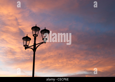 Ornate black street light silhouetted against a pink sunset cloudy sky. Stock Photo