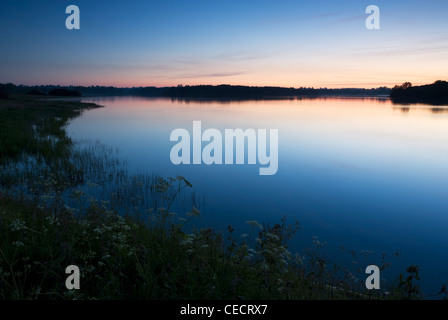 Blue and pink hues of dawn are reflected in the still water of a reservoir Stock Photo