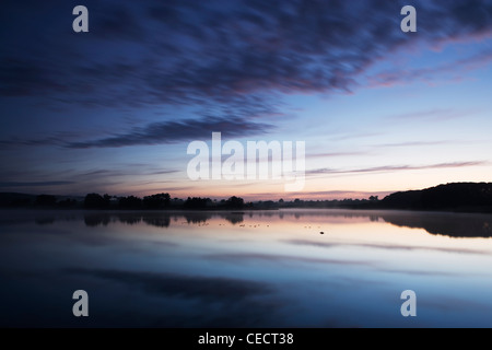 View across Sywell Reservoir at dawn. The sky is reflected in the water and both have taken on shades of blue. Stock Photo