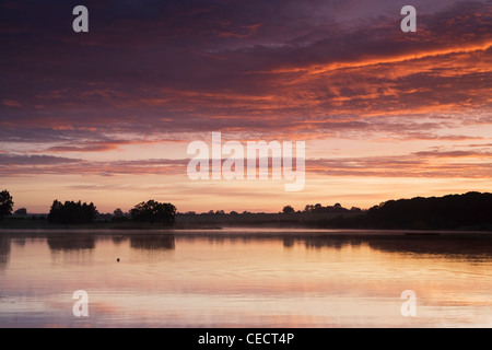 View across Sywell Reservoir at dawn. The sky is reflected in the water and both have taken on shades of pink. Stock Photo