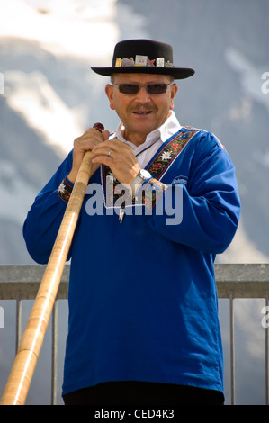 Vertical close up portrait of a traditionally dressed Swiss man holding an Alpine horn on a sunny day. Stock Photo