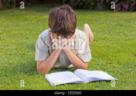 boy reading book on green grass lawn Stock Photo