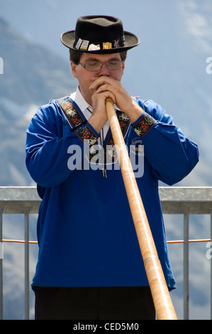 Vertical close up portrait of a traditionally dressed Swiss man playing the Alpine horn on a sunny day. Stock Photo