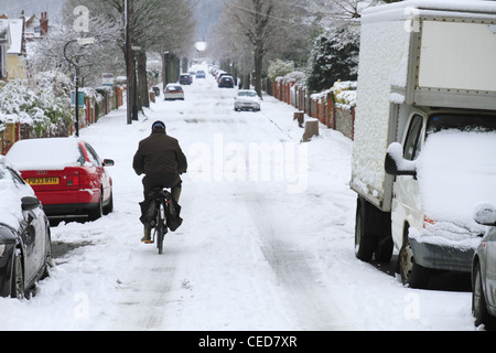 An old elderly man person cycling his bike bicycle uphill up hill in the snow on a snowy street road Eastbourne UK