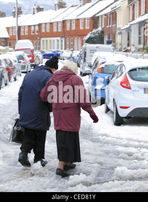 Old elderly people couple man and & woman pensioners walking crossing the road street in snow ice UK dangerous slippery winter Stock Photo
