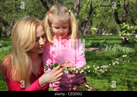 Mother and daughter look at blossoming branch of apple-tree in garden Stock Photo