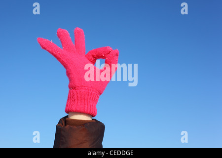 Hand in red glove against  blue sky shows gesture ok Stock Photo