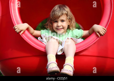 little girl sits in red plastic hole on playground Stock Photo