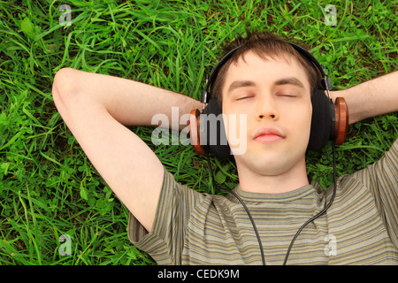 young man lies on grass in headphones