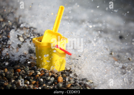 Yellow children's bucket with  scoop on stone seacoast with splashing water Stock Photo