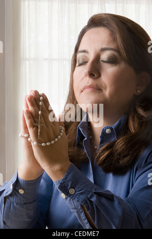 Hispanic woman holding rosary praying Stock Photo