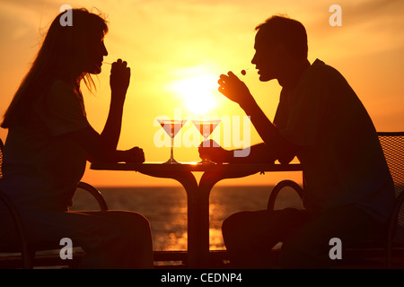 Female and man's silhouettes on sunset sit at table with two glasses and olives outdoor Stock Photo