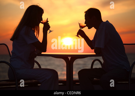 Female and man's silhouettes on sunset behind table drink from glasses Stock Photo