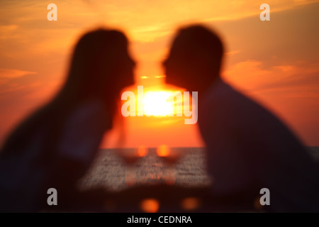 Blurred in boke female and man's silhouettes on sunset sit at table with two glasses outdoor Stock Photo