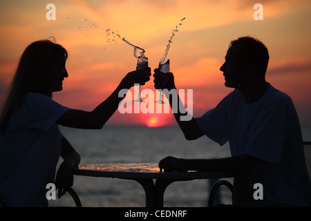 silhouettes of man and woman splash out drink from glass on sea sunset. focus on man Stock Photo