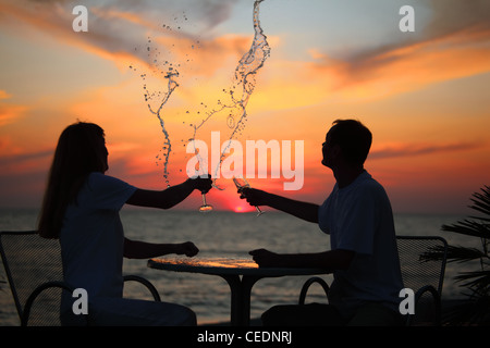 silhouettes of man and woman splash out drink from glass on sea sunset Stock Photo