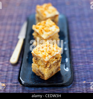 Three white chocolate cake squares topped with white chocolate and chopped walnuts, close-up Stock Photo