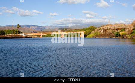 River Waimea flows under road bridge at estuary with canyon in distance Stock Photo