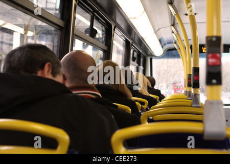 a view, from behind, of people sitting on the top deck of a red London bus as it travels along a road Stock Photo