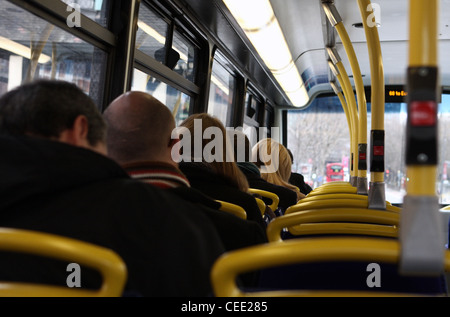 a view, from behind, of people sitting on the top deck of a red London bus as it travels along a road Stock Photo