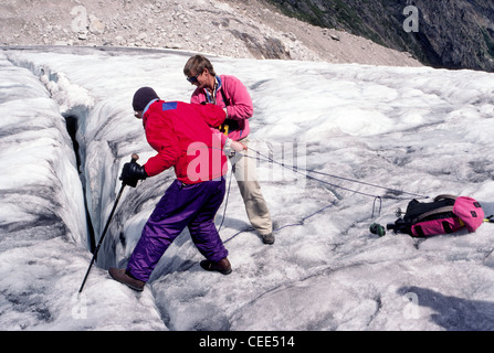 A guide helps a hiker peer into a crevasse on the Malloy Glacier in the Bugaboo range of the ancient Purcell Mountains in British Columbia, Canada. Stock Photo