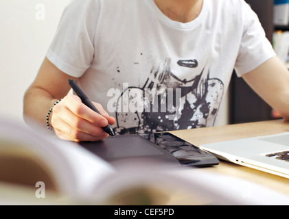 Man using graphics tablet while seated in front of his laptop at a desk. Stock Photo