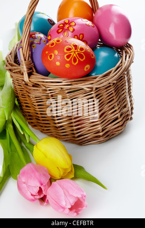 Image of decorative Easter eggs in basket and bunch of tulips near by Stock Photo