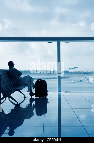 Lady in a lobby airport waiting for her flight, looking through a glass with solar protection. Stock Photo
