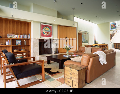 Small vintage pine chest-of drawers used as table beside brown leather sofa in modern living room with wood-framed chairs Stock Photo