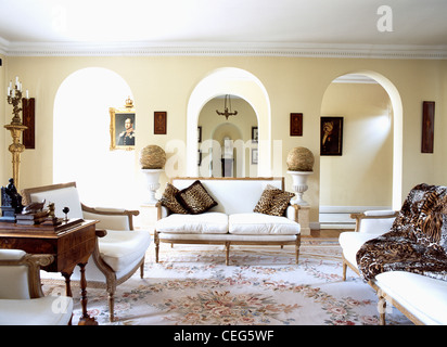 Leopard-print cushions and throw on white French-style sofas in living room with arches to corridor Stock Photo