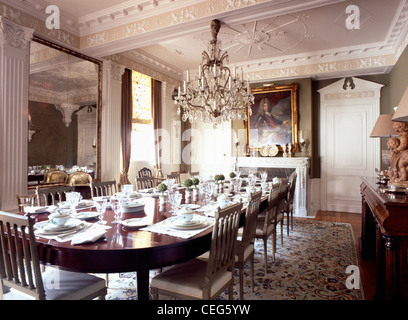 Antique glass chandelier above long antique table set for lunch in large dining room with ornate plasterwork on ceiling Stock Photo