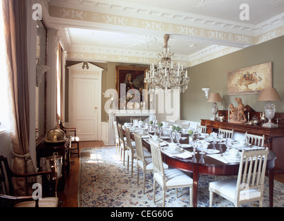 Antique glass chandelier above long antique table set for lunch in spacious dining room with ornate plasterwork on ceiling Stock Photo