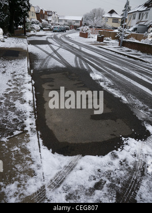 Clear patch of road after parked car has moved off following night of snowfall Stock Photo
