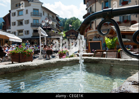 Water fountain and street cafes in Megève village. Haute-Savoie department Rhône-Alpes region south-eastern France. Stock Photo