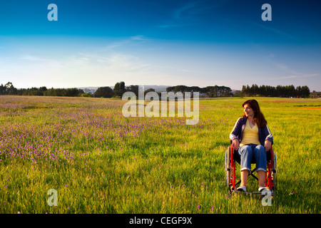 Happy handicapped woman on a wheelchair over a green meadow looking away Stock Photo