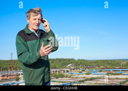 Mature Caucasian man in working clothes speaking on cellphone outdoor Stock Photo