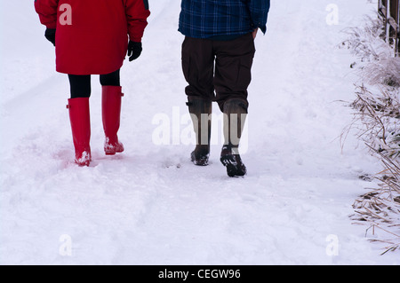 People Couple Rear View Of Walking Through The Snow Wearing Wellington Boots Winter UK Stock Photo